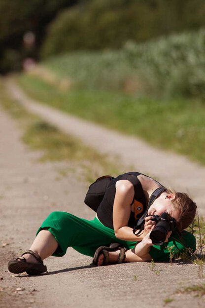 Frau fotografiert beim Fotokurs liegend am Weg eine Blume