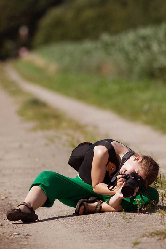 Frau fotografiert liegend am Weg eine Blume